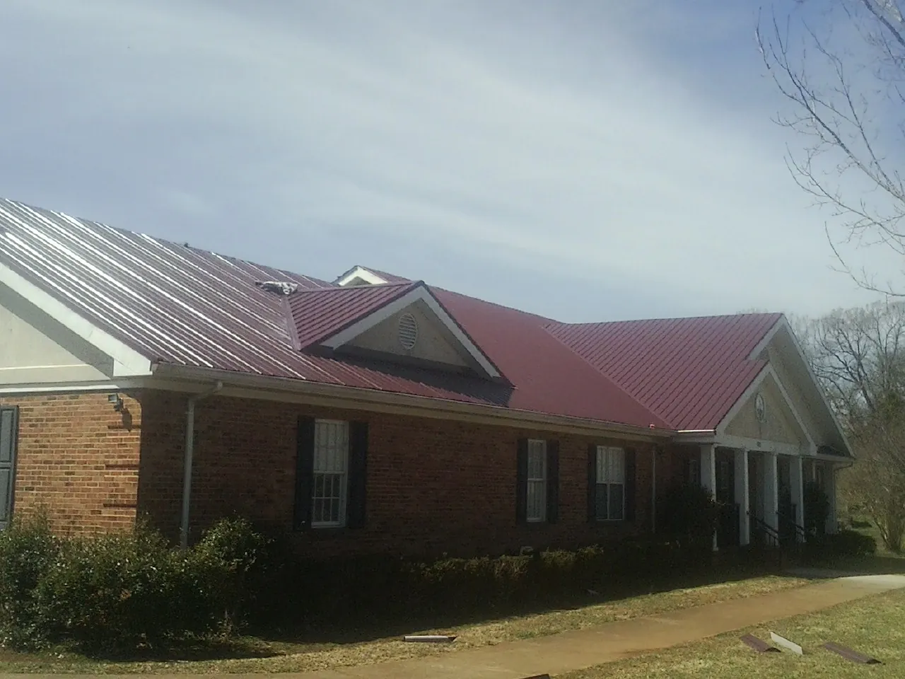 Red metal roof with gabled entries on a long brick building, from a Hail Damage Roof Repair job in Dauphin
