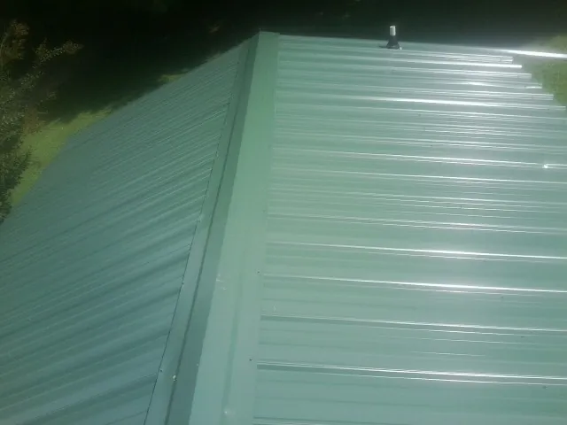 New green metal panels meeting at the ridge of a roof — Flat Roof Repair work by our crew in Dauphin