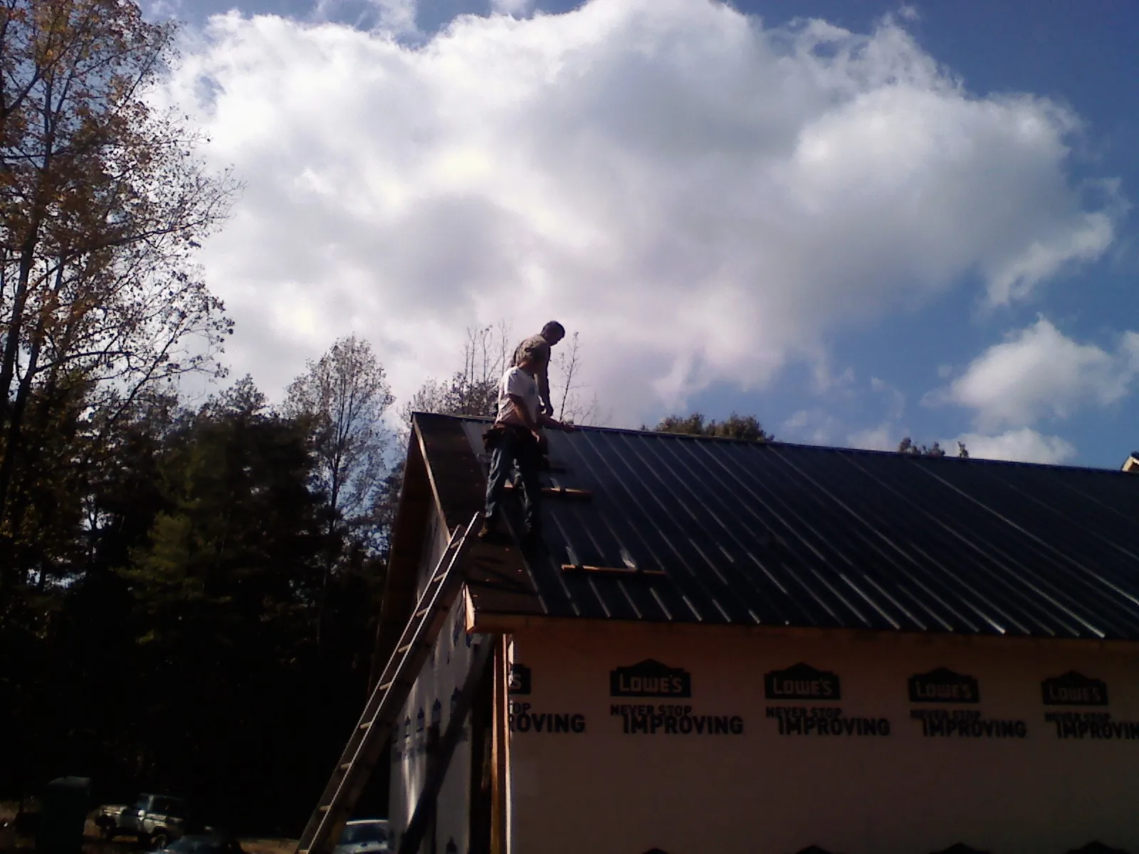 Roofer fastening dark metal panels high against a cloudy sky, from a Roof Inspection job in Dauphin