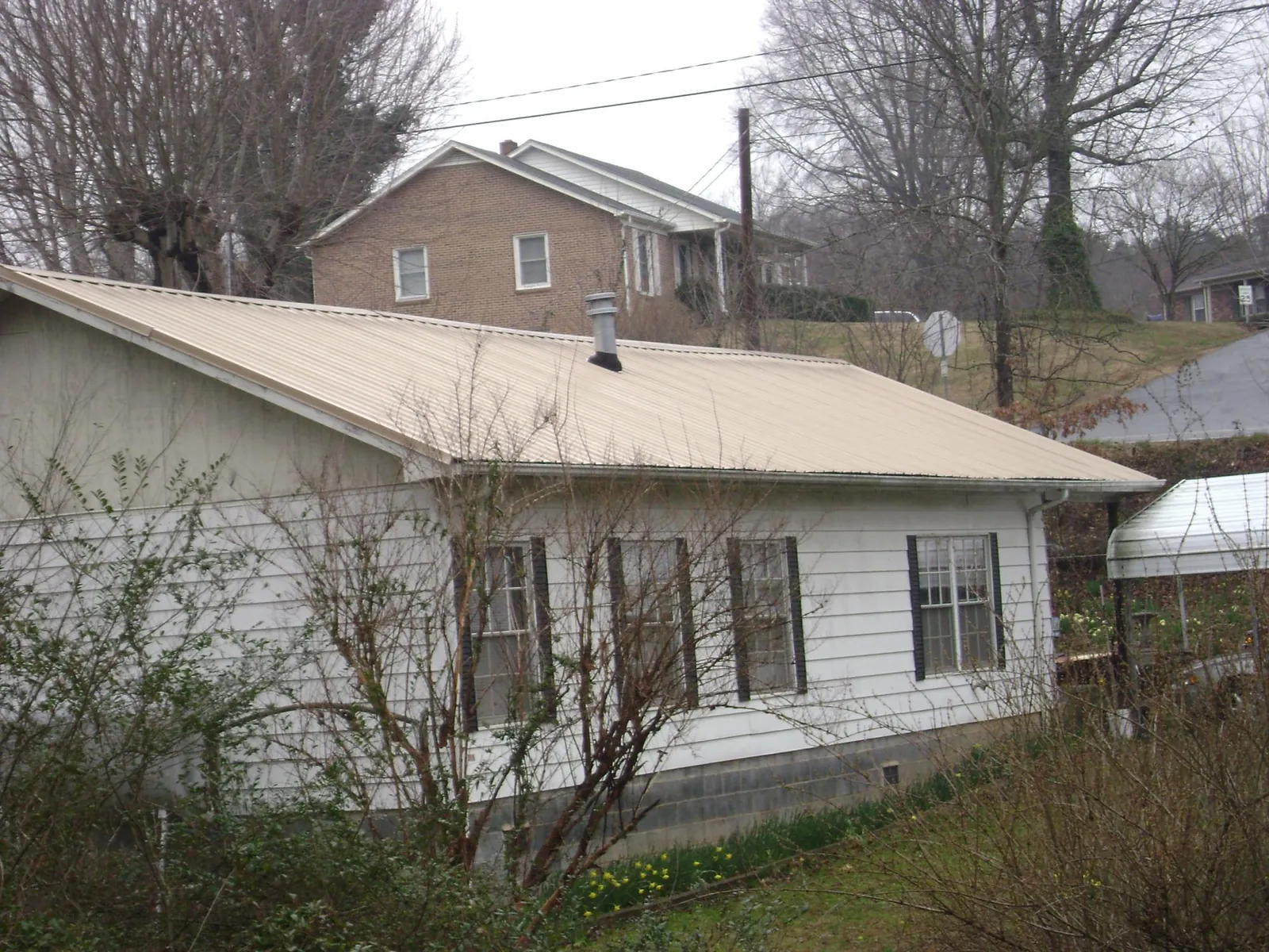 Tan metal roof on a white sided house set into a hillside — Commercial Roofing by Roofing Brothers in Dauphin