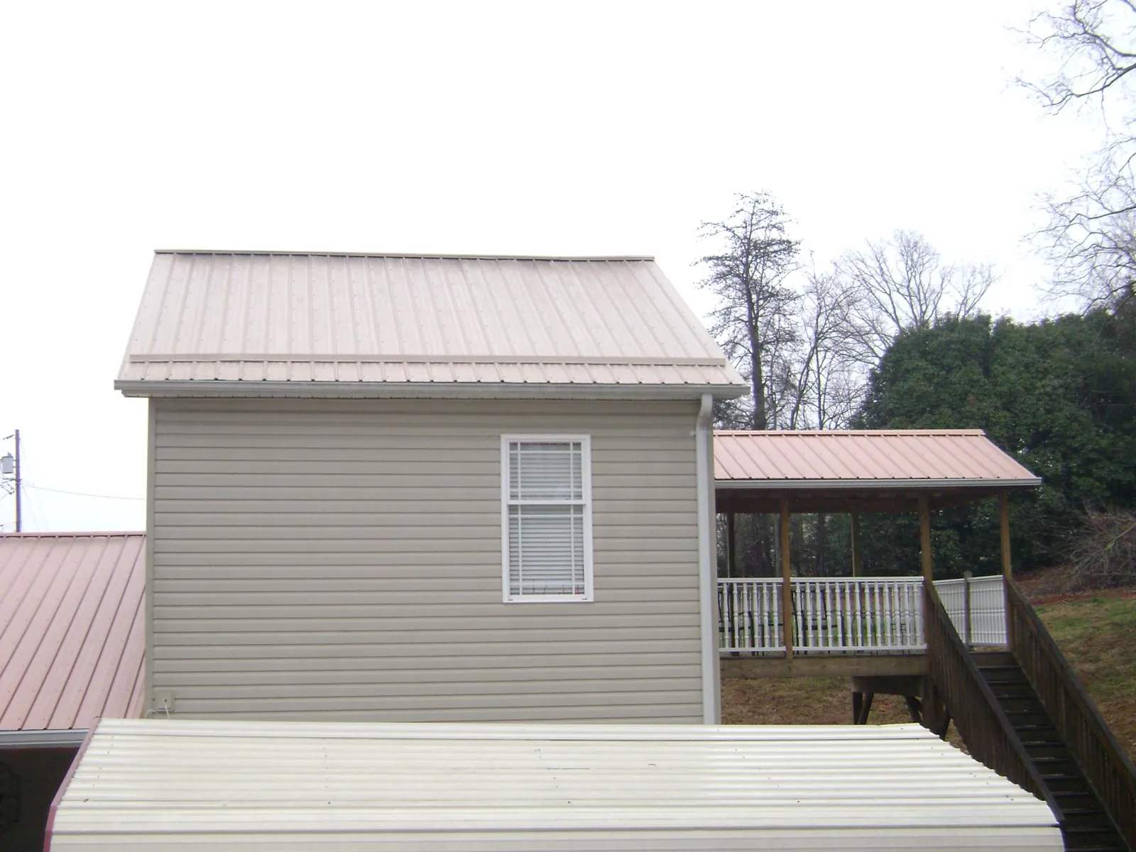 Tan metal roofs on a two story addition and attached porch, from a Roof Replacement job in Dauphin